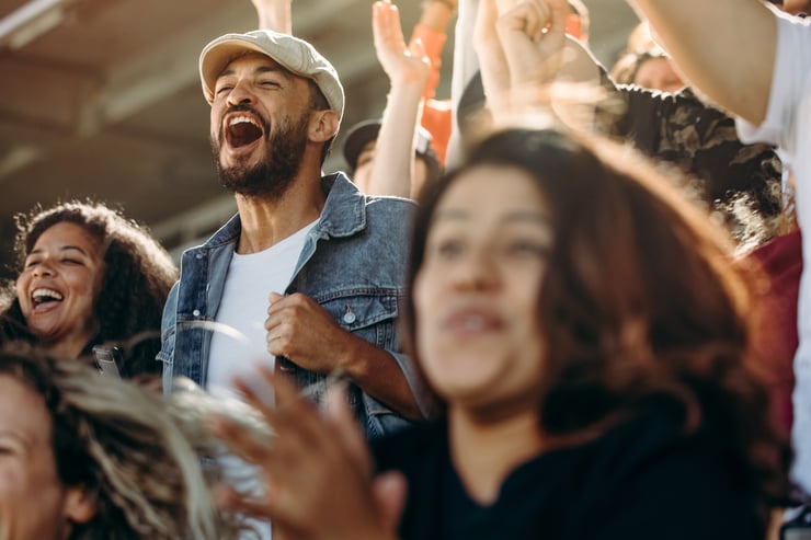 A crowd of ecstatic fans is cheering loudly and celebrating in the bleachers of a youth sports game.