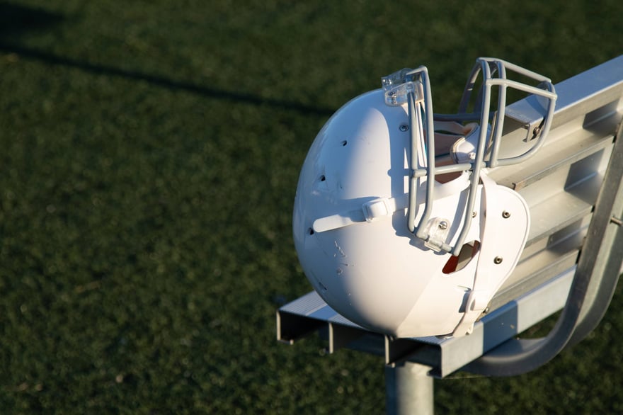 Football helmet on a sideline bench, capturing the quiet moment of a multi-sport athlete transition on the field.